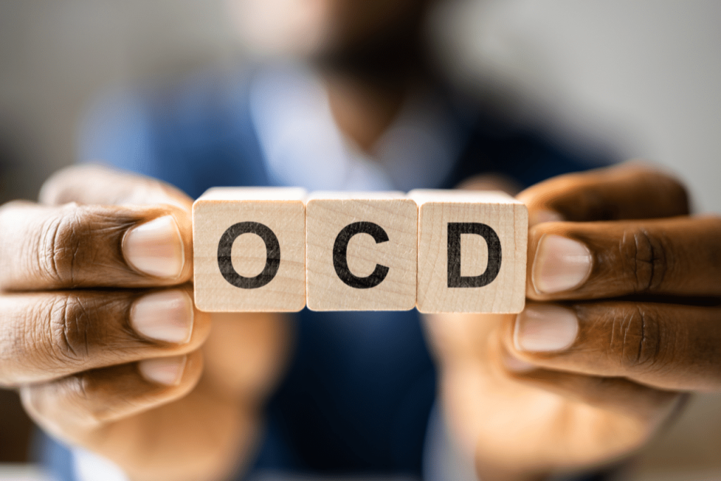 man holding up a sign that says ocd when answering What is OCD Caused By?|What is OCD Caused By?|||||||woman sitting with her therapist discussing What is OCD Caused By?|woman struggling with OCD