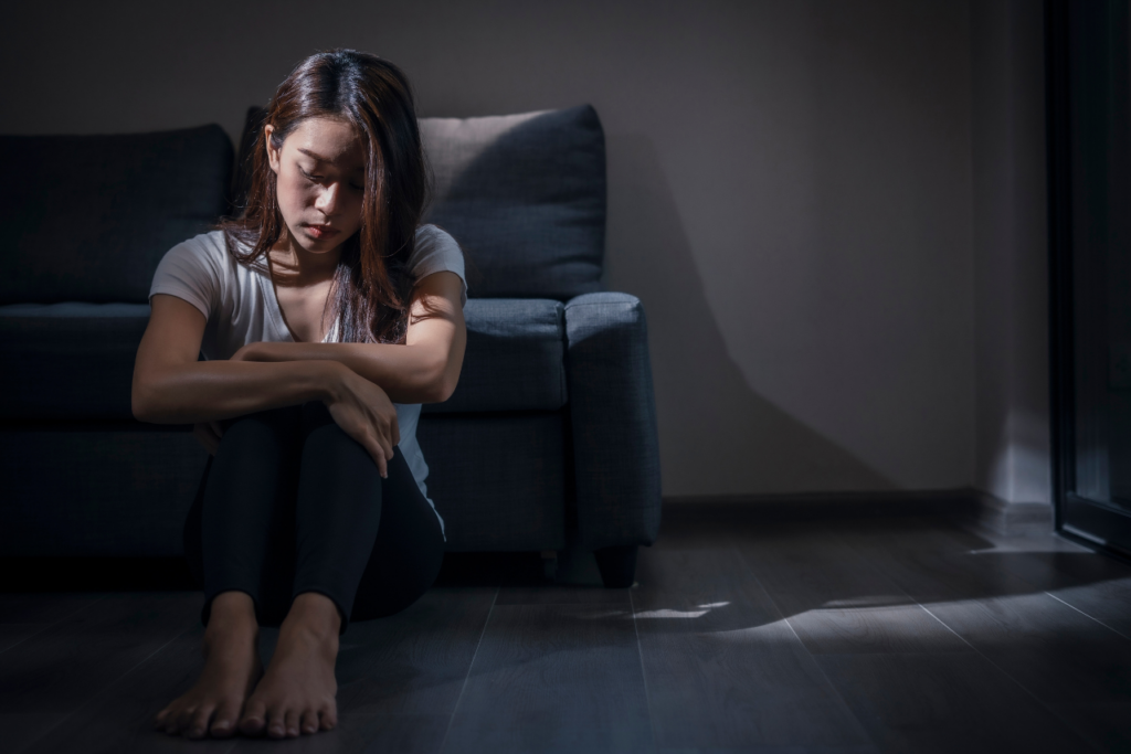 woman sitting on the floor in the dark wondering why do people cut themselves