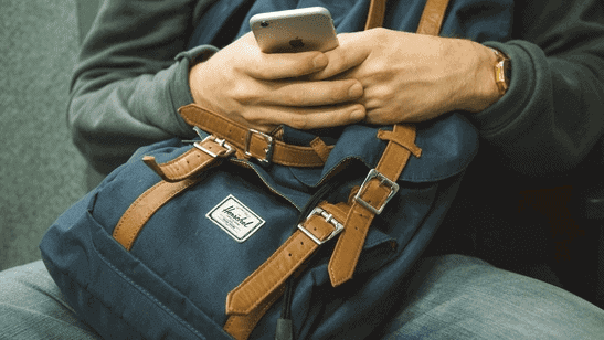 Alt Text: An image of a person holding an iPhone as their hands rest on a blue bag. | Self-Harm | The Meadowglade|Two Women | Self Harm | The Meadowglade