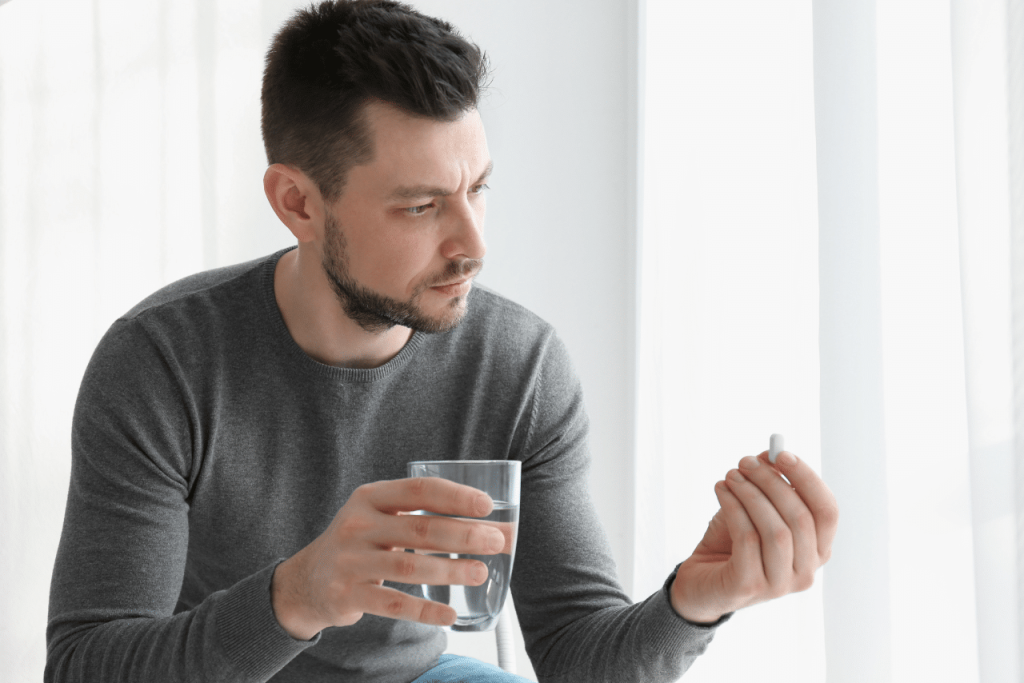 man holding a glass of water and a pill showing Signs Your Antidepressant dose is too low