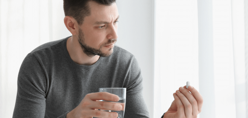 man holding a glass of water and a pill showing Signs Your Antidepressant dose is too low