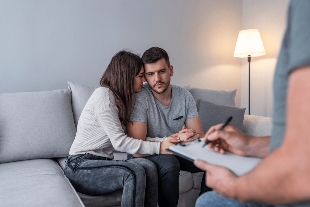 mother and father of newborn baby speaking to their therapist asking father holding his new born baby wondering can men get postpartum depression?