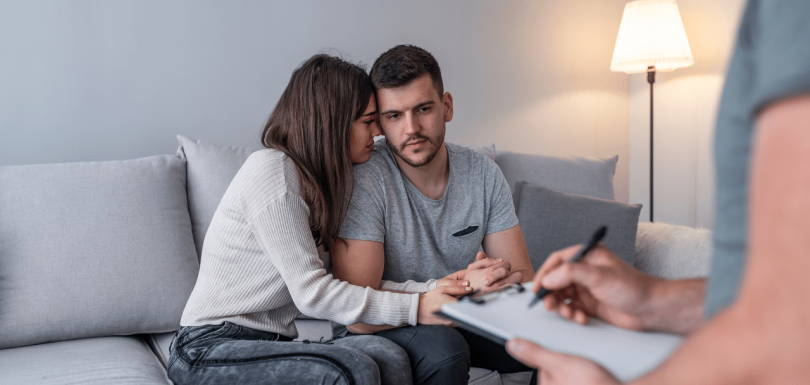 mother and father of newborn baby speaking to their therapist asking father holding his new born baby wondering can men get postpartum depression?