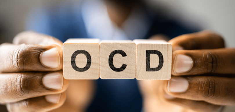 man holding up a sign that says ocd when answering What is OCD Caused By?|What is OCD Caused By?|||||||woman sitting with her therapist discussing What is OCD Caused By?|woman struggling with OCD