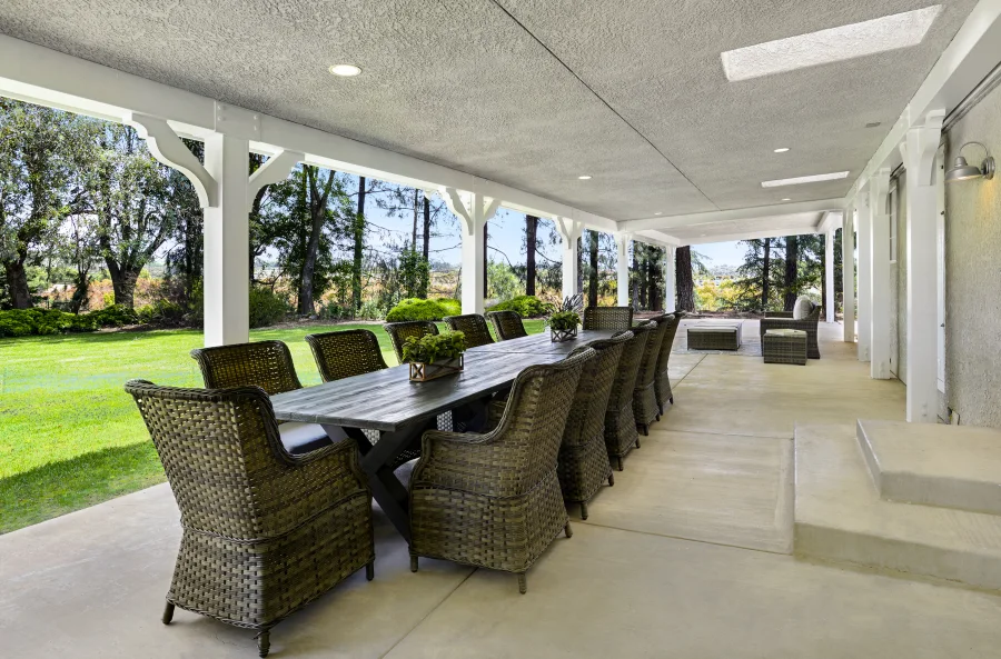 Long outdoor dining table on the residential cottage covered terrace overlooking the garden