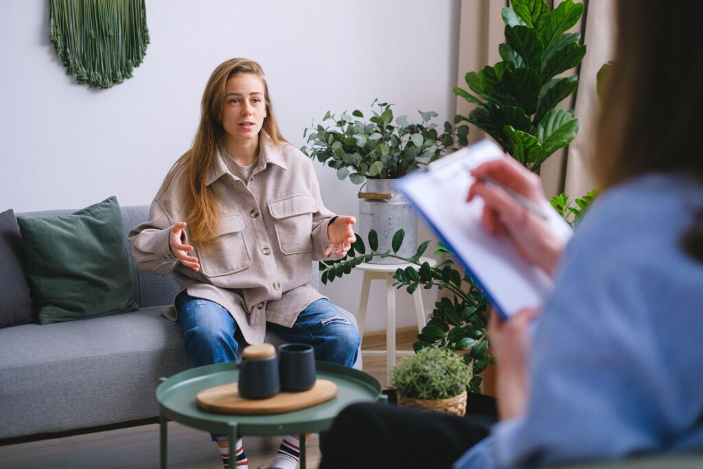 A client talks on a sofa in a bright living room while a therapist takes notes.