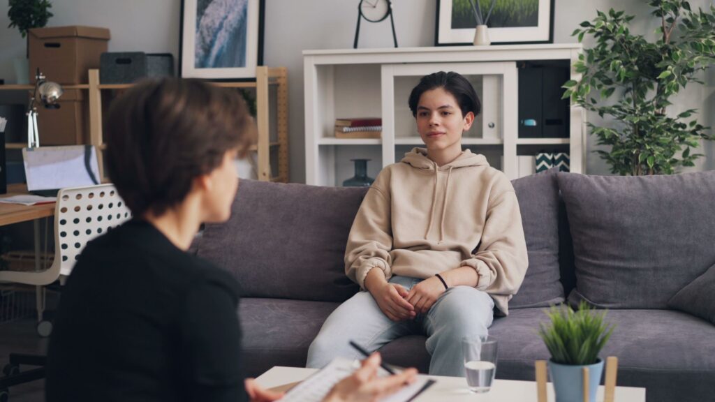 A client talks with a therapist on a grey sofa in a homey room.