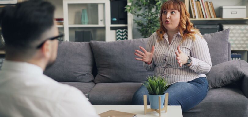 A client talks with a therapist on a grey sofa
