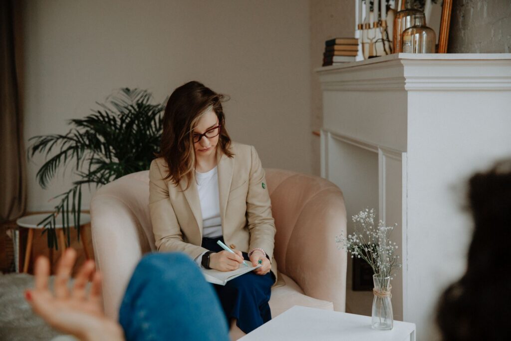 A therapist takes notes in an armchair while a client talks