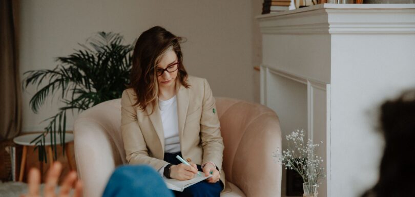 A therapist takes notes in an armchair while a client talks