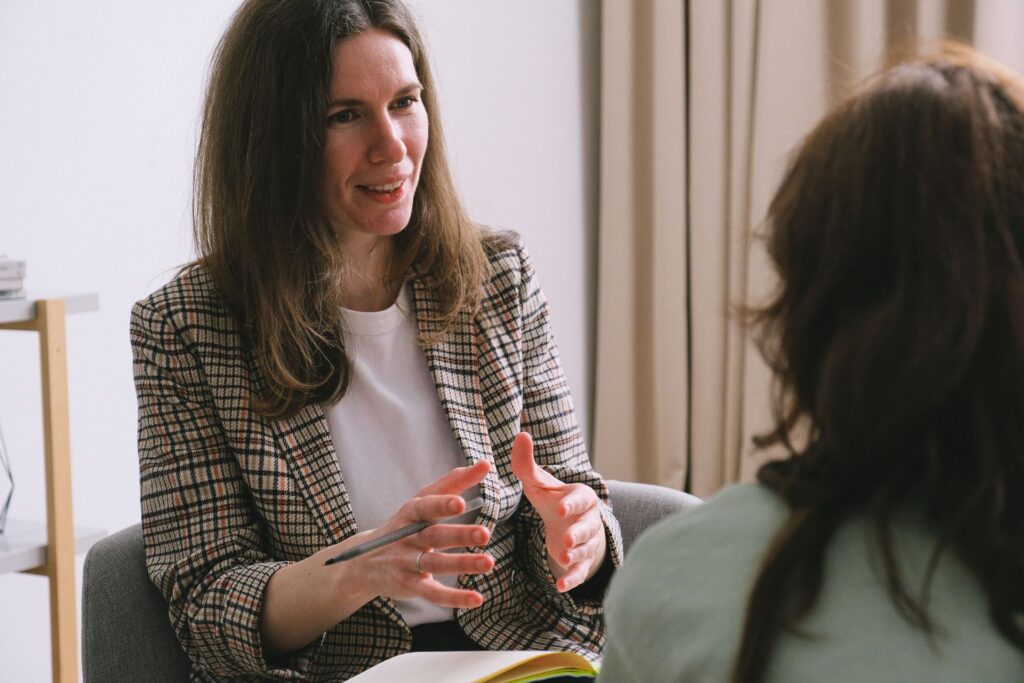 A woman talks with a therapist in a warm, softly lit room.